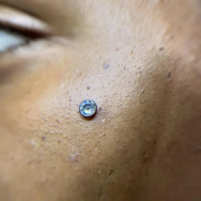 Microdermal com pedra clara no rosto, perto do olho